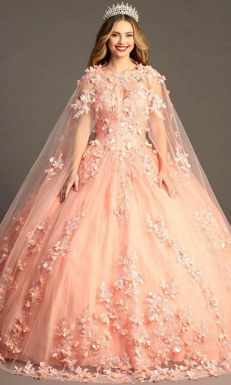 A woman stands against a plain background wearing the Quinceanera Dress CHF3055 By Chicas—a peach-colored, glitter tulle ballgown adorned with 3D floral appliques and a cape—paired with a silver tiara.